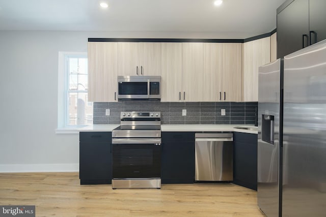 kitchen with appliances with stainless steel finishes, light brown cabinets, light hardwood / wood-style floors, and backsplash