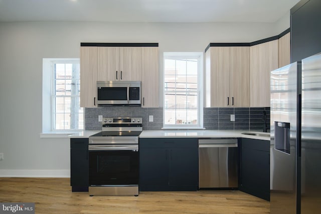 kitchen with appliances with stainless steel finishes, light wood-type flooring, tasteful backsplash, and light brown cabinets