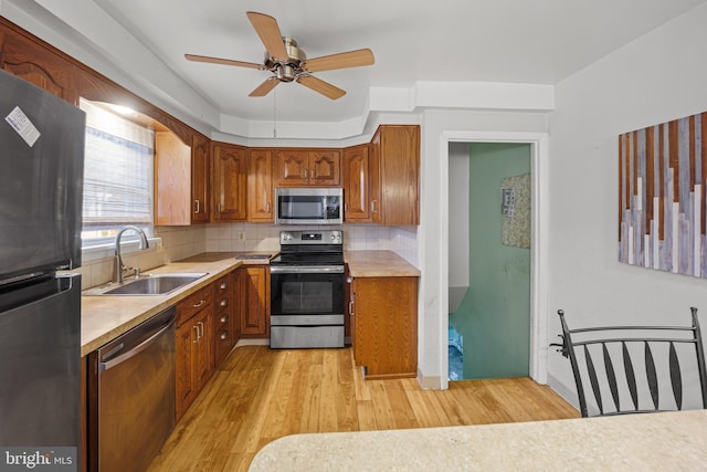 kitchen with ceiling fan, sink, stainless steel appliances, decorative backsplash, and light wood-type flooring