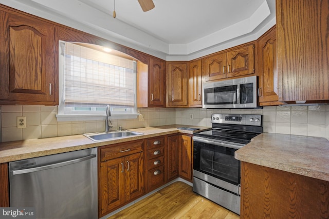 kitchen with ceiling fan, sink, stainless steel appliances, light hardwood / wood-style floors, and decorative backsplash