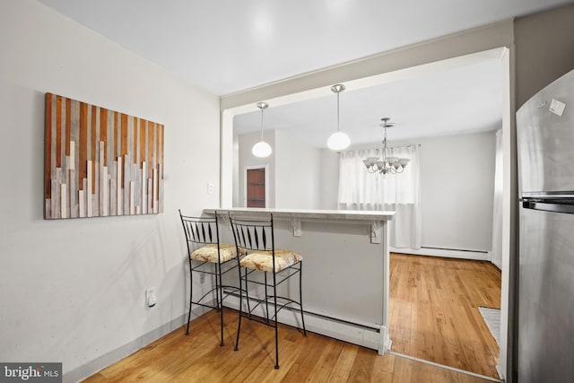 kitchen featuring a breakfast bar, baseboard heating, decorative light fixtures, a notable chandelier, and stainless steel refrigerator