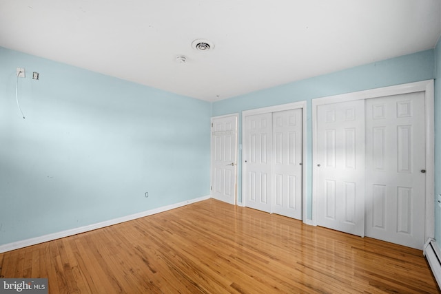 unfurnished bedroom featuring a baseboard radiator, two closets, and wood-type flooring