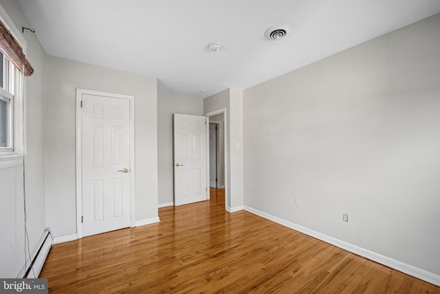 unfurnished bedroom with hardwood / wood-style floors and a baseboard heating unit