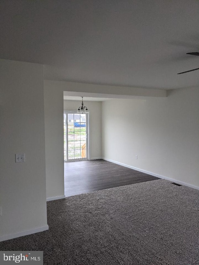 unfurnished room with ceiling fan with notable chandelier and dark carpet