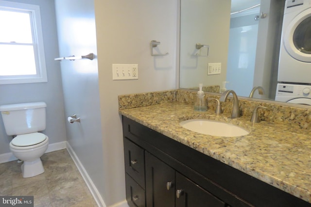 bathroom with a healthy amount of sunlight, vanity, toilet, and stacked washer and clothes dryer