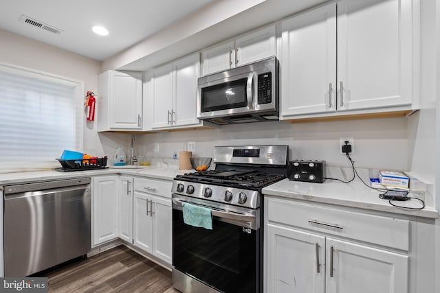 kitchen with dark wood-type flooring, appliances with stainless steel finishes, light stone counters, and white cabinets