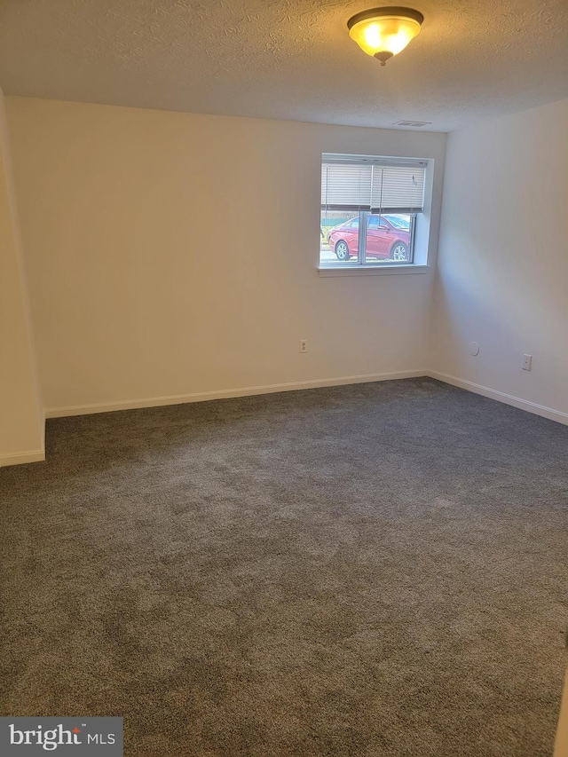 spare room featuring baseboards, visible vents, dark carpet, and a textured ceiling