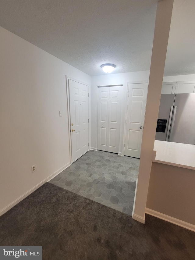 entryway featuring dark colored carpet, a textured ceiling, and baseboards