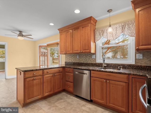 kitchen with brown cabinets, dark stone countertops, a peninsula, stainless steel dishwasher, and a sink