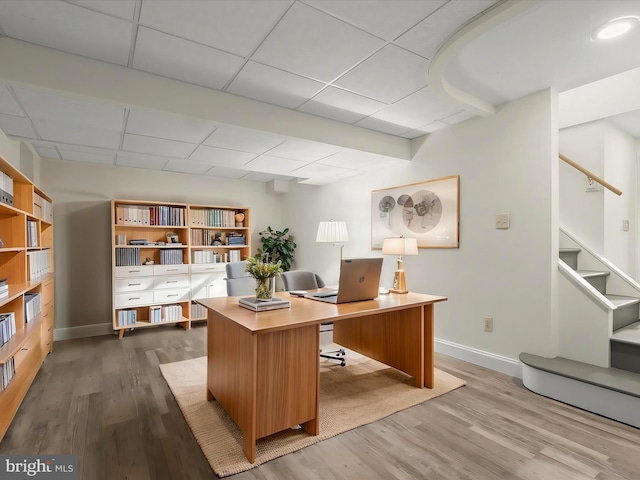 home office featuring baseboards, a drop ceiling, and wood finished floors