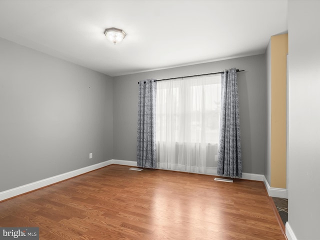 empty room featuring baseboards, visible vents, and wood finished floors