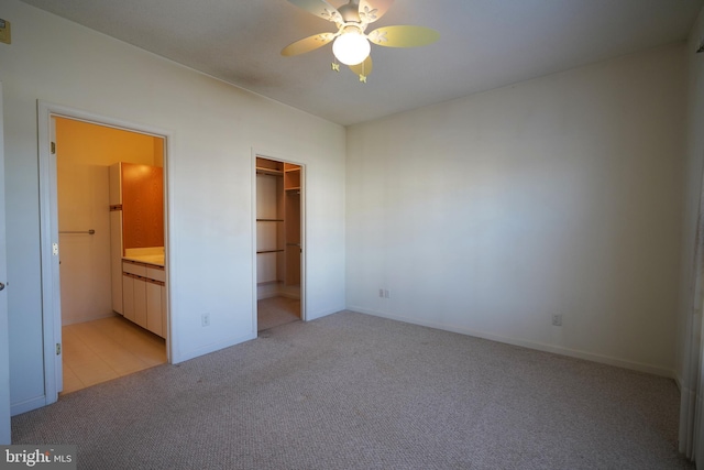 unfurnished bedroom featuring ensuite bathroom, light colored carpet, ceiling fan, a spacious closet, and a closet