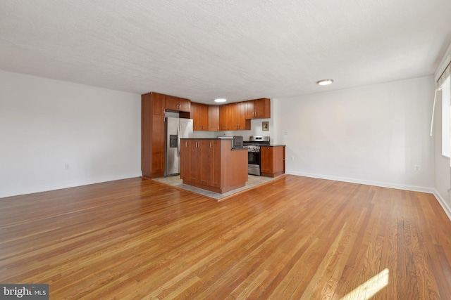 kitchen with stainless steel appliances, a textured ceiling, a kitchen island, and light hardwood / wood-style flooring