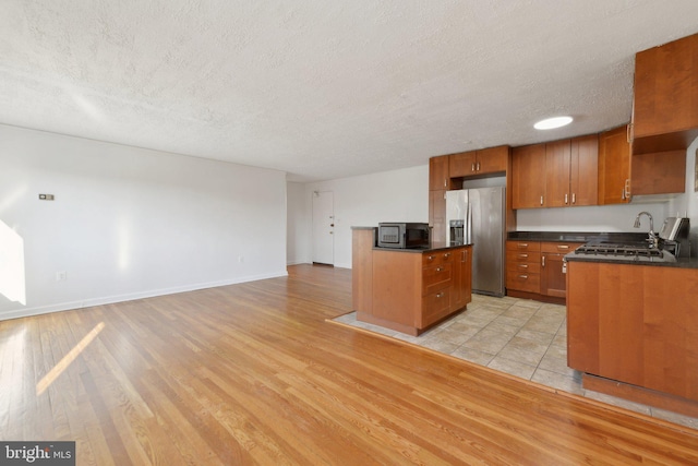 kitchen with appliances with stainless steel finishes, a kitchen island, light hardwood / wood-style flooring, and a textured ceiling