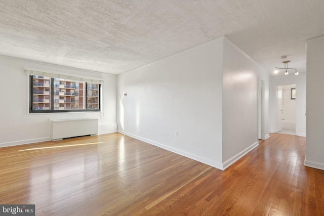 spare room with a textured ceiling, radiator heating unit, and wood-type flooring