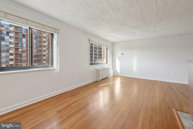 spare room with hardwood / wood-style floors, radiator heating unit, and a textured ceiling