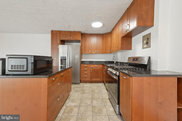 kitchen with appliances with stainless steel finishes, sink, light tile patterned floors, and a textured ceiling