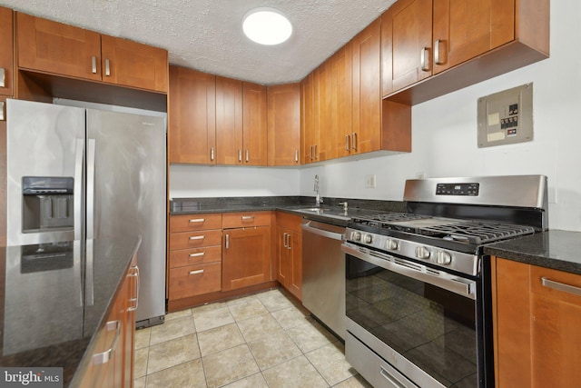 kitchen with sink, dark stone counters, light tile patterned floors, stainless steel appliances, and a textured ceiling