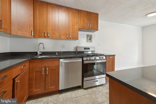 kitchen with sink, light tile patterned floors, dark stone countertops, stainless steel appliances, and a textured ceiling