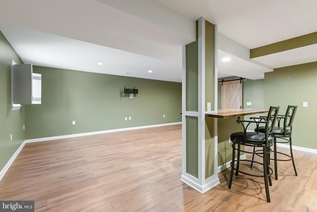 kitchen featuring a kitchen bar, a barn door, butcher block countertops, and light hardwood / wood-style flooring