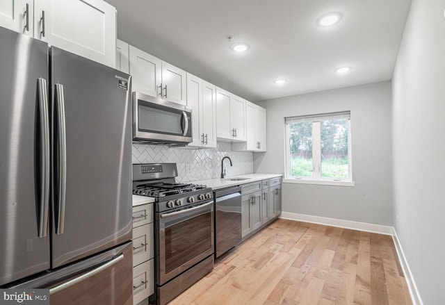 kitchen featuring backsplash, sink, light hardwood / wood-style flooring, white cabinetry, and stainless steel appliances