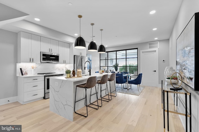 kitchen featuring decorative light fixtures, white cabinetry, stainless steel appliances, and an island with sink