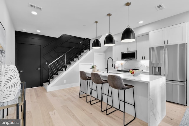 kitchen featuring stainless steel appliances, white cabinetry, hanging light fixtures, and a kitchen island with sink