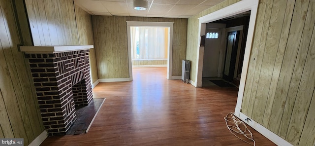 interior space featuring a drop ceiling, radiator heating unit, a brick fireplace, hardwood / wood-style floors, and wooden walls