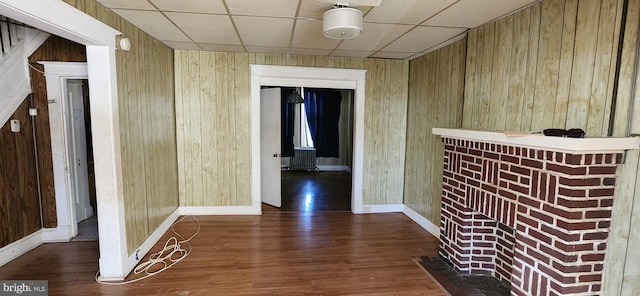 hall featuring dark hardwood / wood-style floors, a drop ceiling, and wood walls