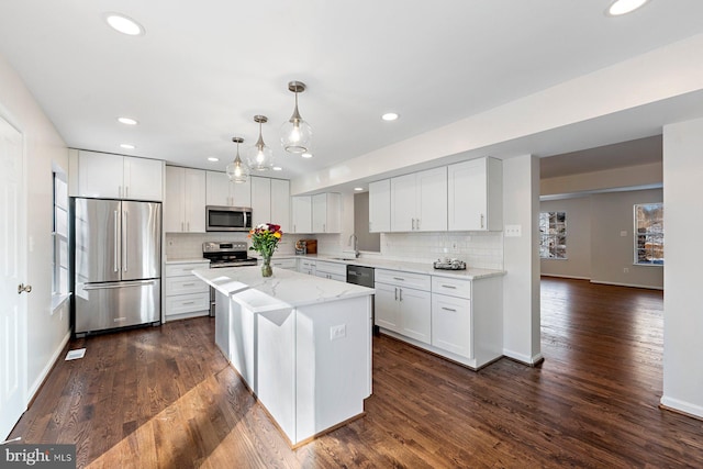 kitchen with light stone countertops, pendant lighting, a kitchen island, white cabinetry, and stainless steel appliances