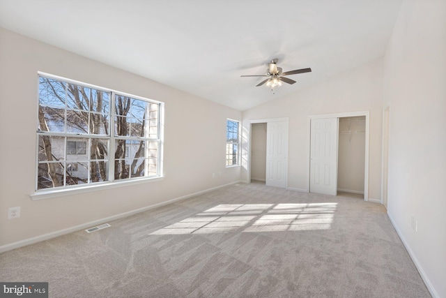 unfurnished bedroom with ceiling fan, two closets, light colored carpet, and vaulted ceiling