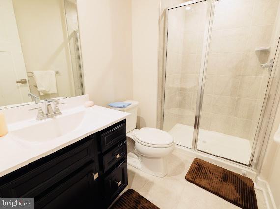 bathroom featuring tile patterned floors, vanity, a shower with shower door, and toilet