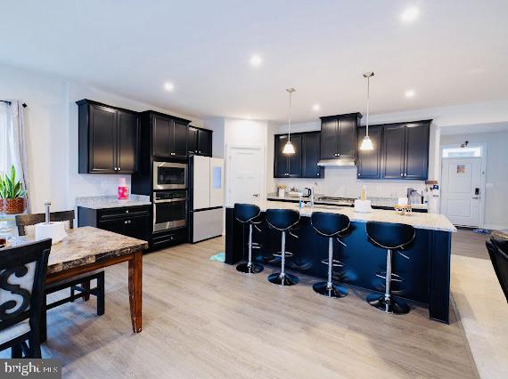 kitchen featuring appliances with stainless steel finishes, light wood-type flooring, a kitchen breakfast bar, decorative light fixtures, and an island with sink