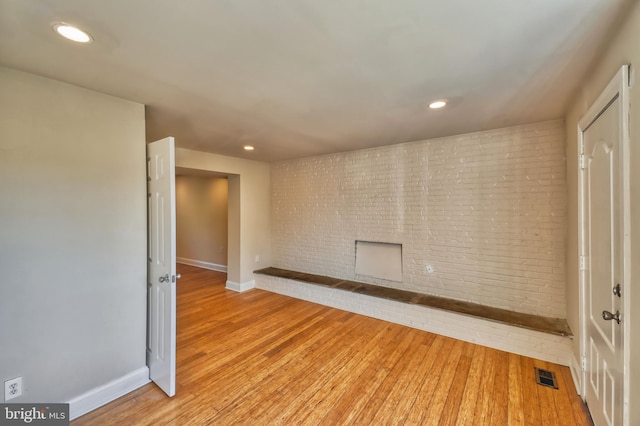 spare room featuring light hardwood / wood-style floors, a fireplace, and brick wall