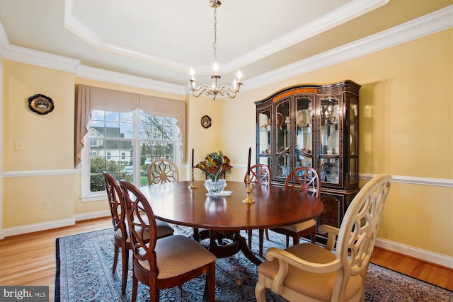 dining area with a tray ceiling, crown molding, a chandelier, and light wood-type flooring