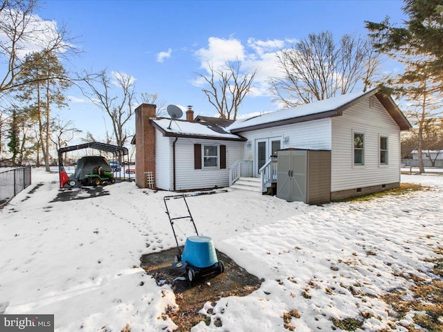 snow covered rear of property featuring a carport and a storage shed