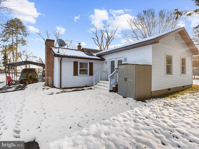 snow covered back of property with a storage unit and a carport