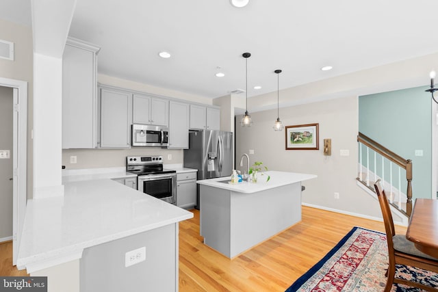 kitchen with appliances with stainless steel finishes, a kitchen island with sink, sink, pendant lighting, and light hardwood / wood-style flooring