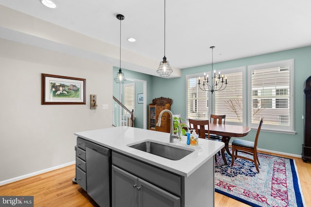 kitchen featuring gray cabinetry, sink, hanging light fixtures, stainless steel dishwasher, and a center island with sink