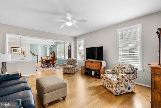 living room with ceiling fan with notable chandelier, light hardwood / wood-style floors, and sink