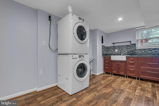 laundry room with sink, dark wood-type flooring, and stacked washing maching and dryer