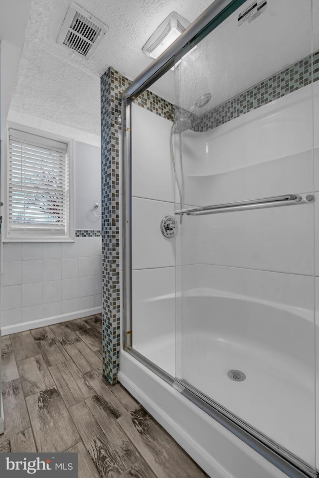 bathroom with hardwood / wood-style flooring, an enclosed shower, and a textured ceiling