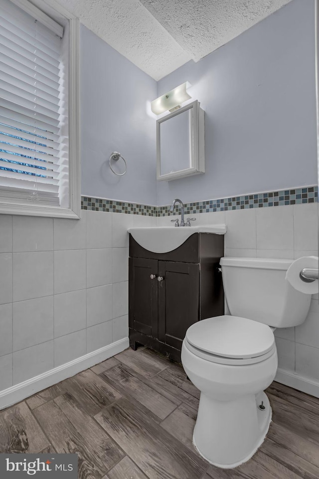 bathroom featuring toilet, a textured ceiling, tile walls, vanity, and hardwood / wood-style flooring