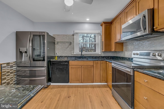 kitchen featuring sink, dark stone counters, light wood-type flooring, stainless steel appliances, and backsplash