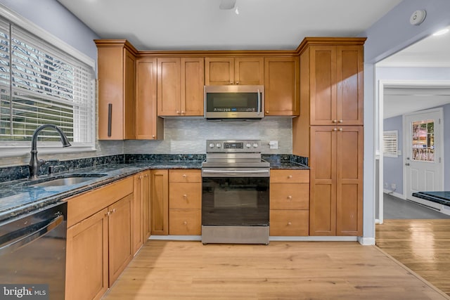 kitchen featuring dark stone countertops, sink, light hardwood / wood-style floors, and appliances with stainless steel finishes