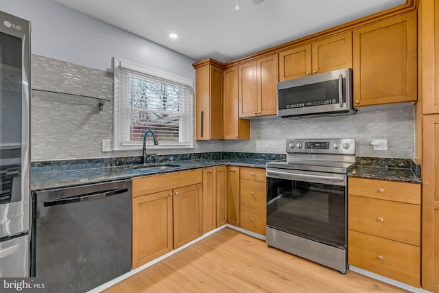 kitchen featuring sink, stainless steel appliances, light hardwood / wood-style floors, decorative backsplash, and dark stone counters