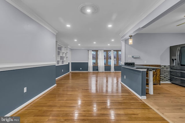 kitchen with stainless steel refrigerator with ice dispenser, a kitchen bar, decorative light fixtures, ornamental molding, and hardwood / wood-style flooring