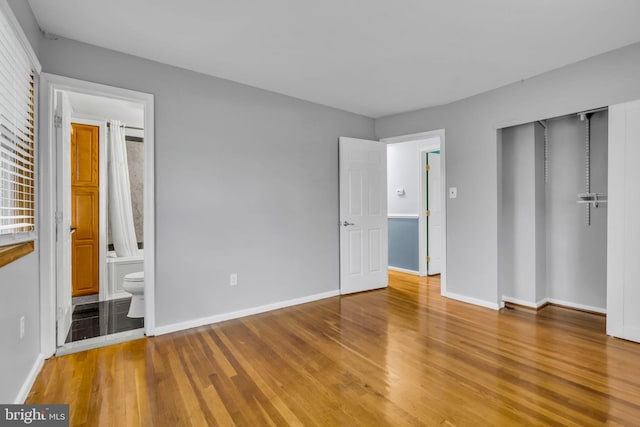 unfurnished bedroom with ensuite bath, wood-type flooring, and a closet