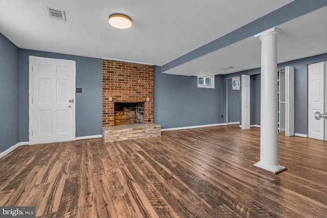 unfurnished living room featuring a brick fireplace, dark wood-type flooring, and ornate columns