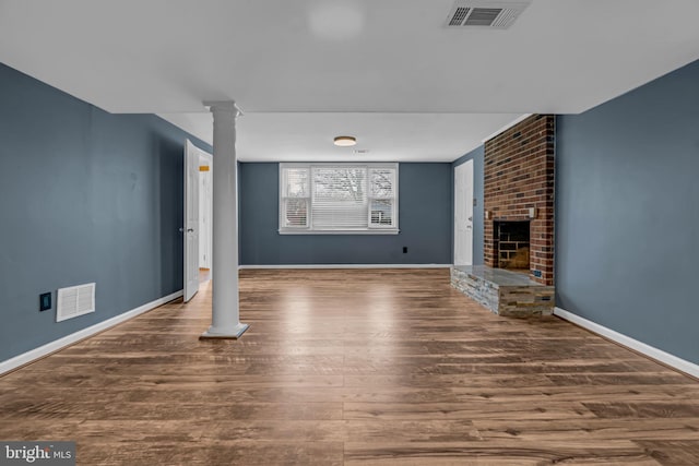 unfurnished living room featuring dark wood-type flooring, a fireplace, and ornate columns